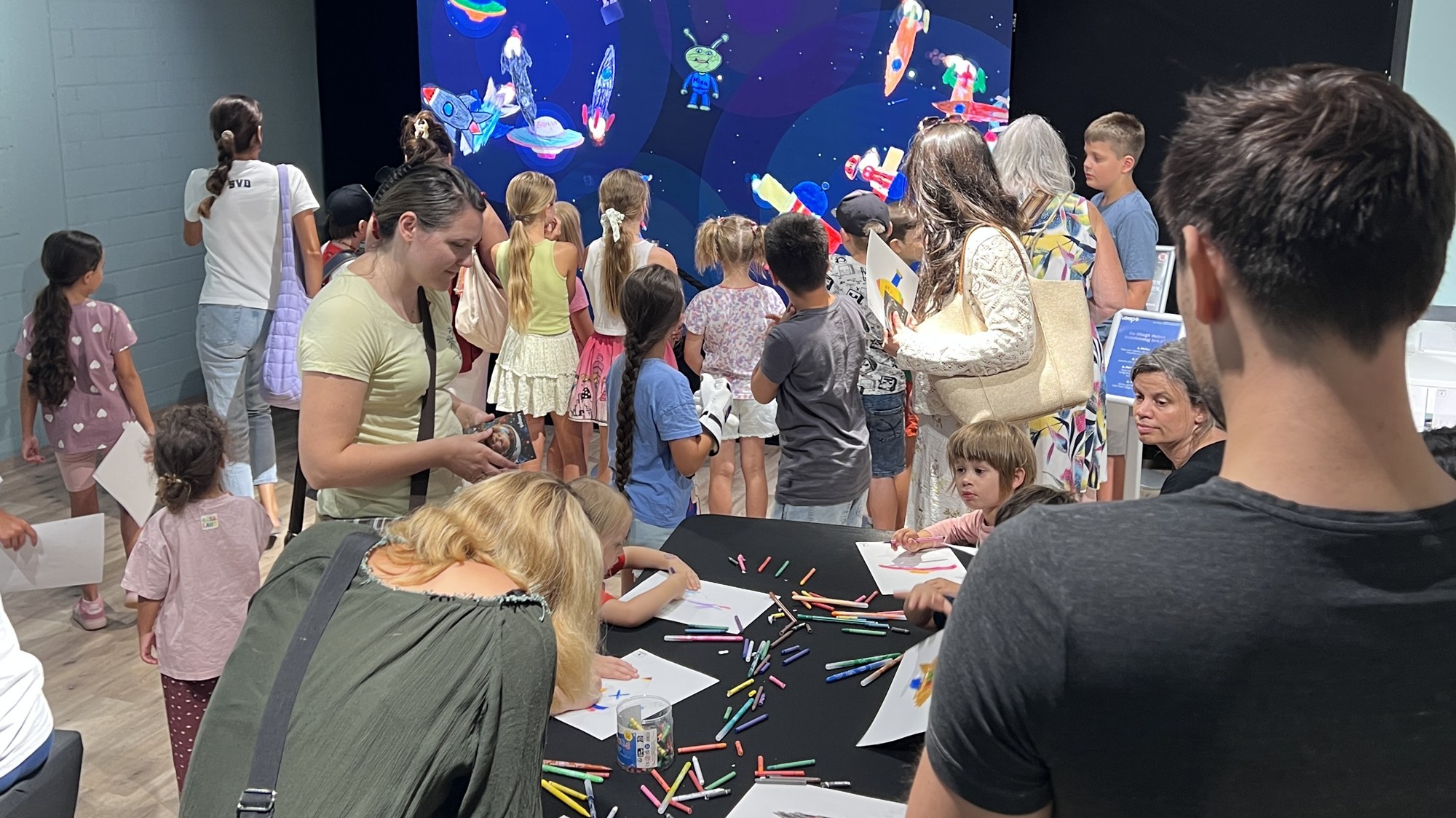 Kinder malen am Maltisch, dahinter die leuchtende Magic Wall